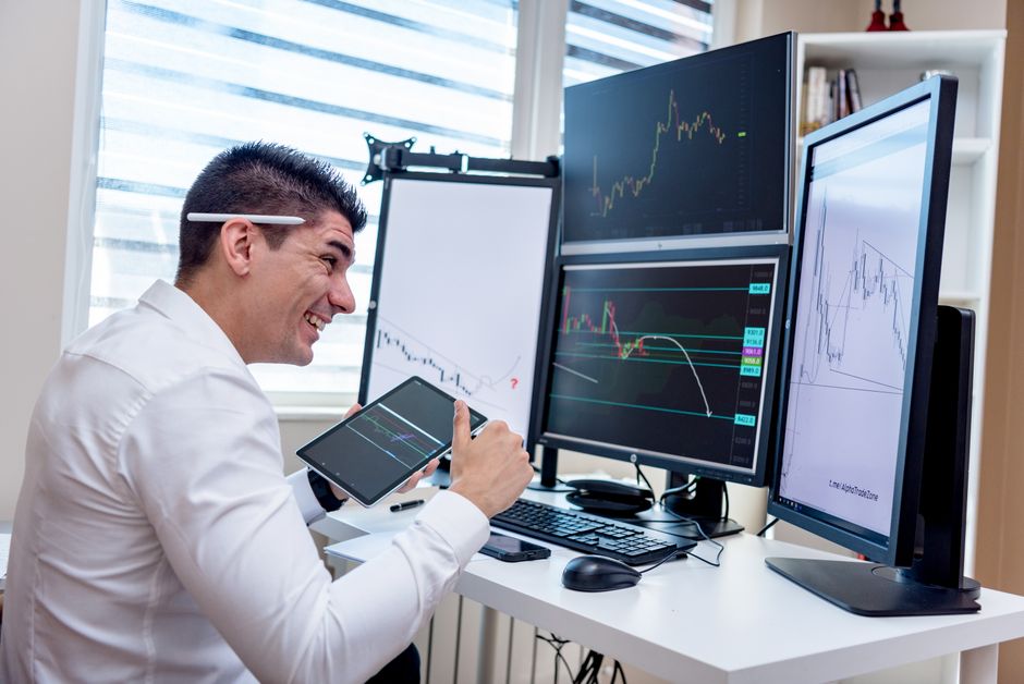 A man engaged in financial data analysis on multiple monitors in an office setting.